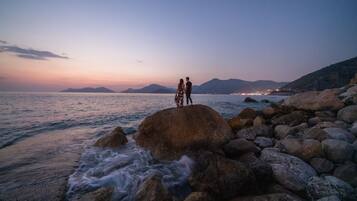 Una pareja está de pie sobre un saliente rocoso frente al mar al atardecer.