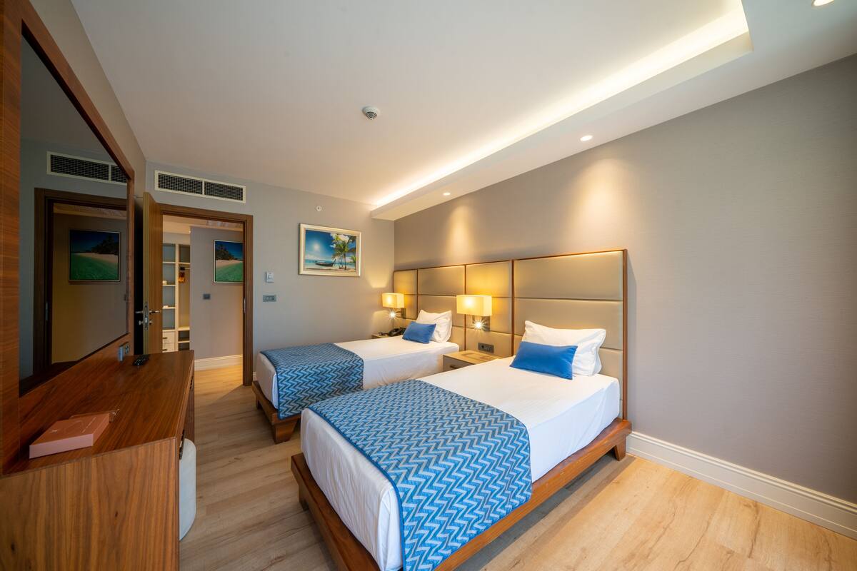A hotel room with two beds, a wooden desk, and a mirror.