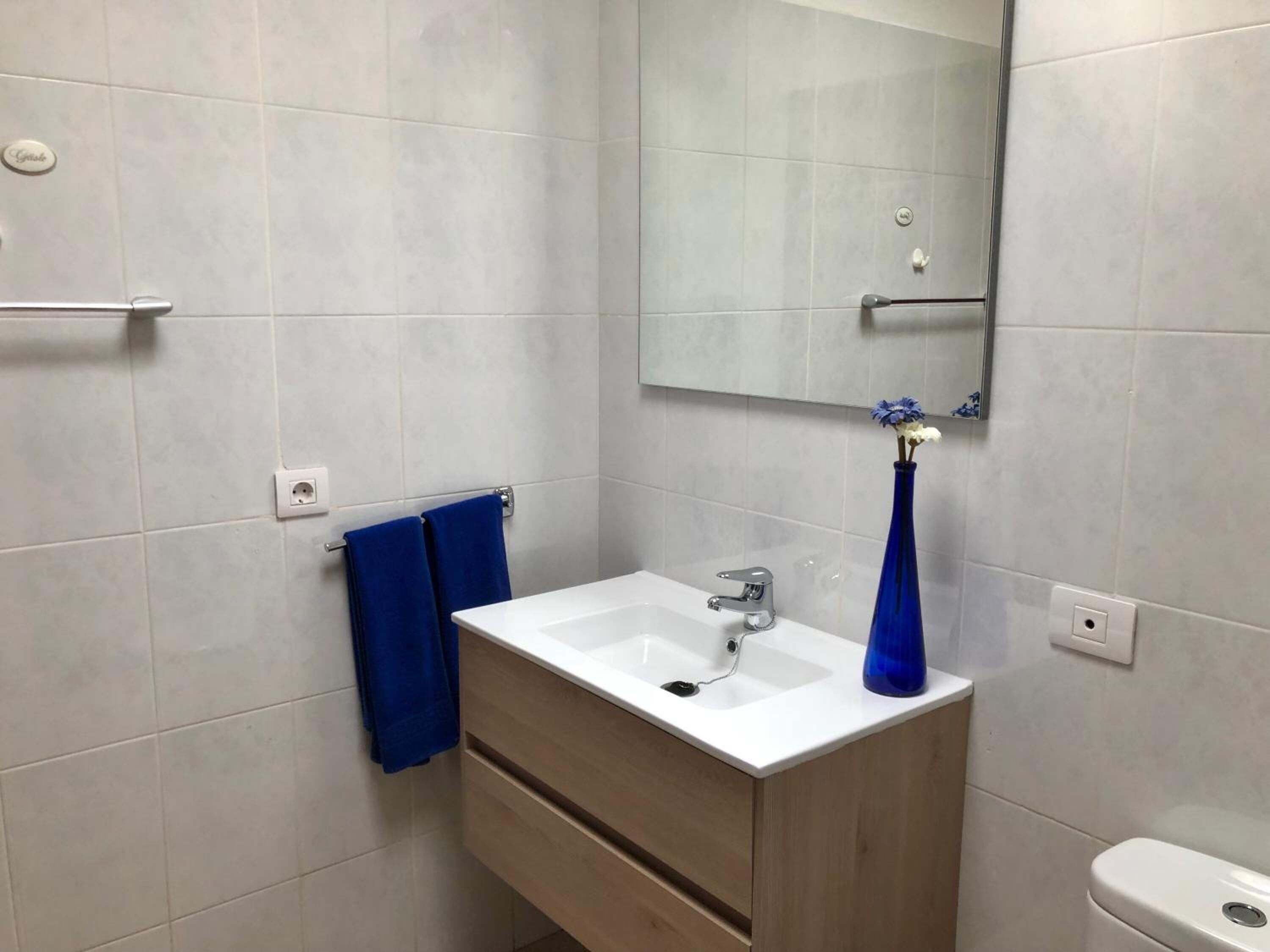 Un baño con un lavamanos blanco, un espejo y un jarrón azul.