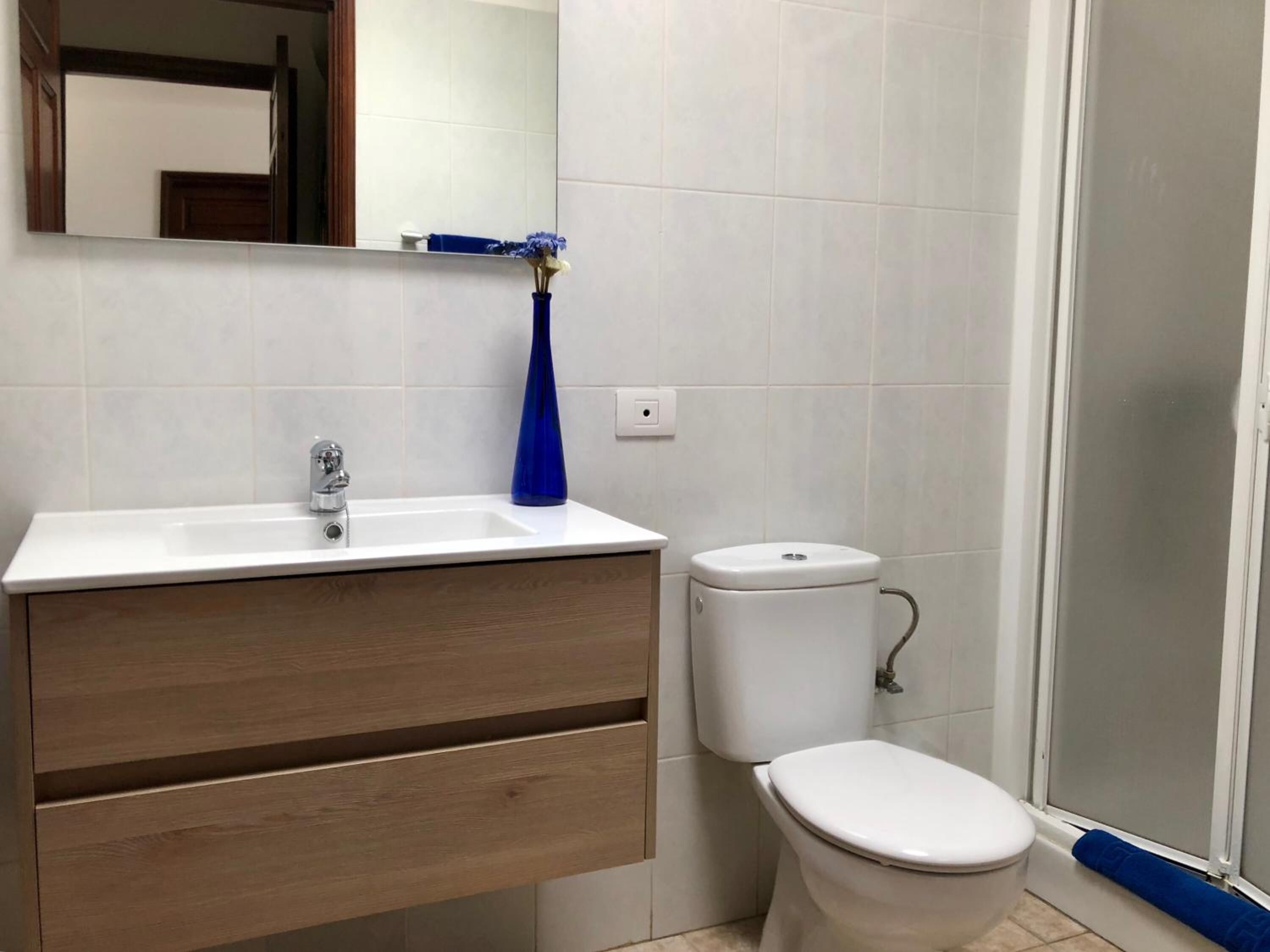 A bathroom with a white sink, wooden vanity, a toilet, and a shower area.