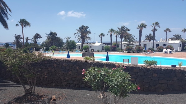 A pool area with a stone wall, palm trees, and lounge chairs. - Casas DEL SOL Bungalows (Yaiza)