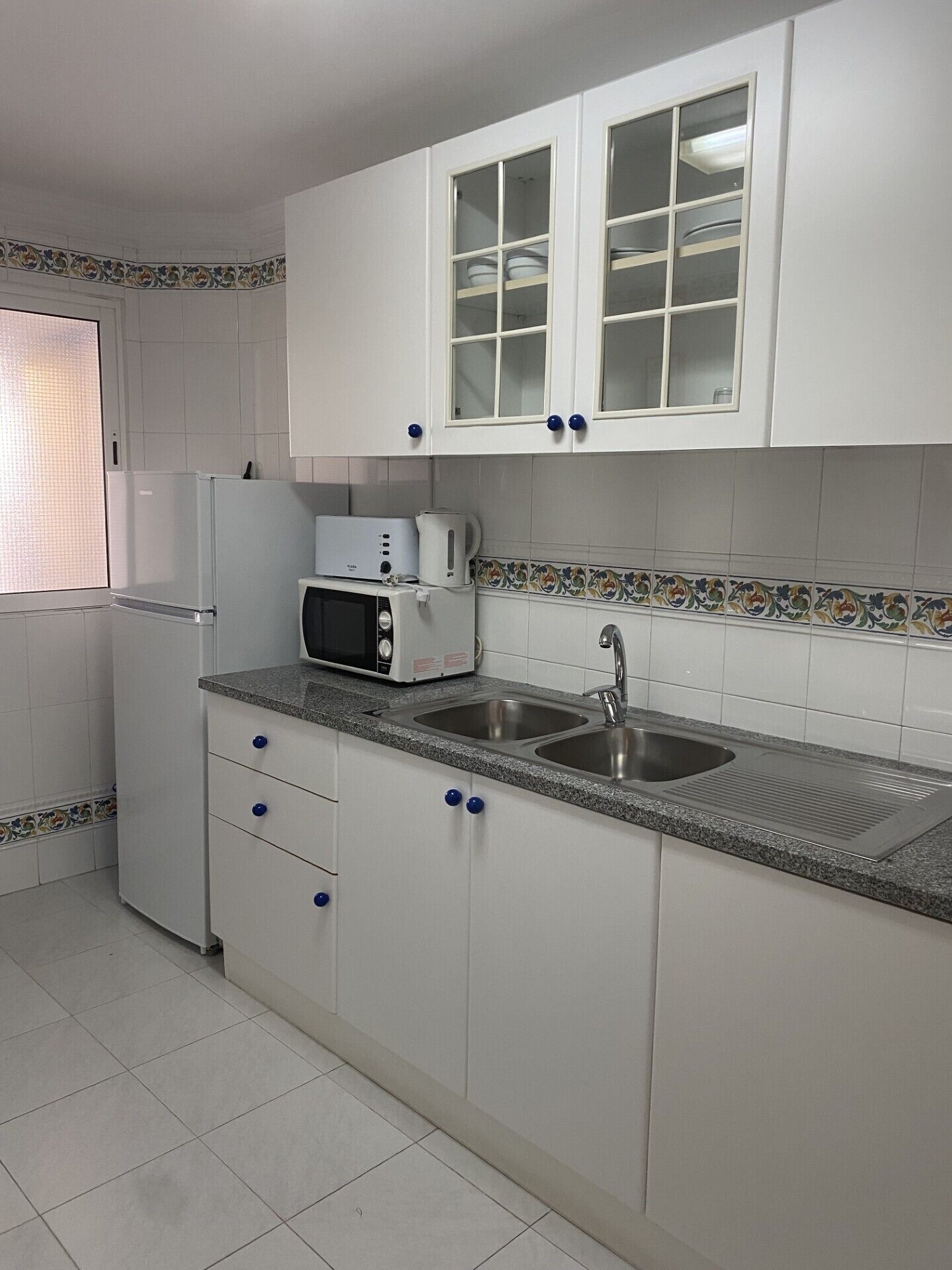 Una cocina con armarios blancos, un microondas, un refrigerador y un lavamanos.