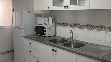 Una cocina con armarios blancos, un microondas, un refrigerador y un lavamanos.