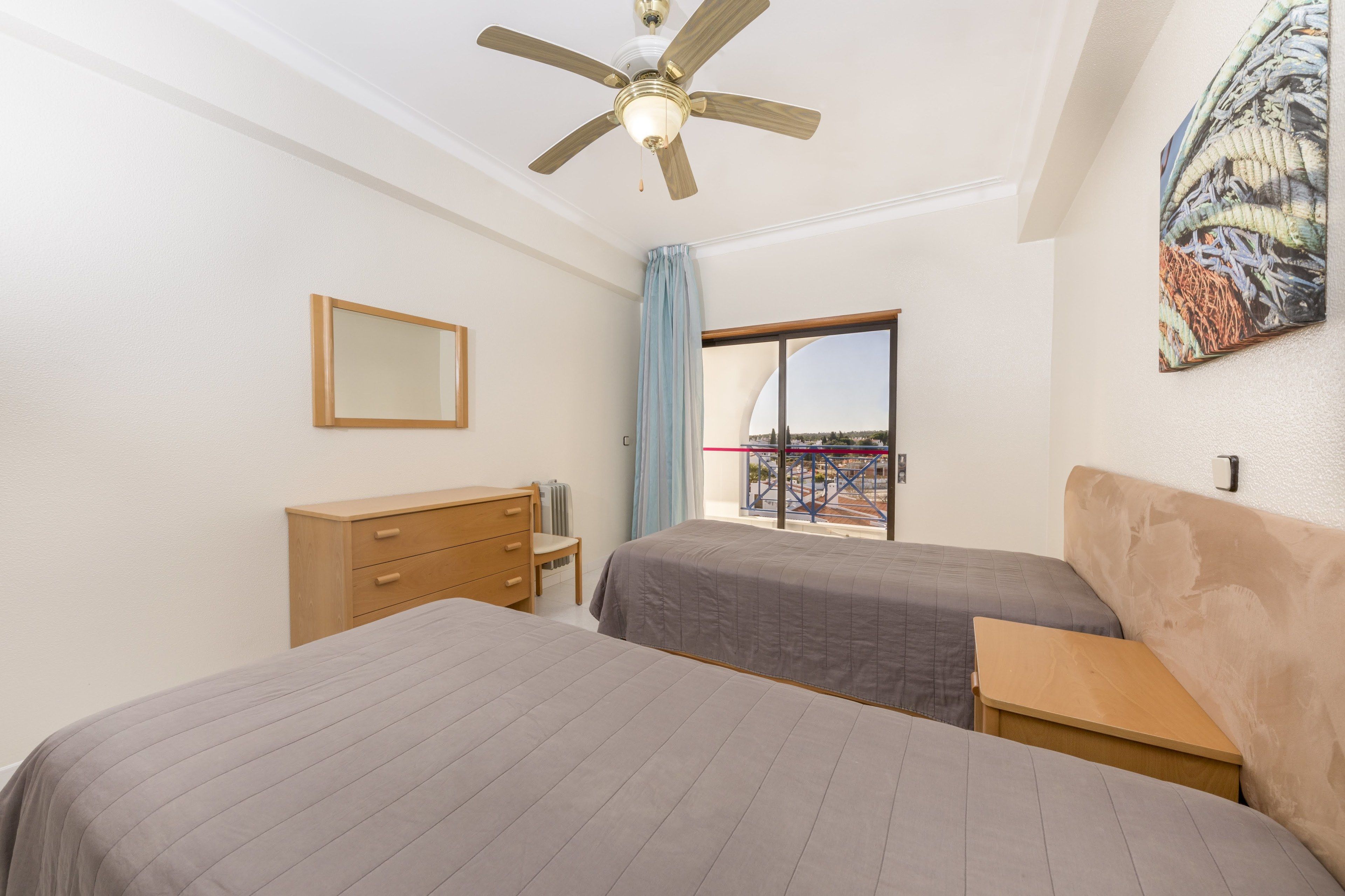 Une chambre d’hôtel avec deux lits, un ventilateur de plafond, une fenêtre donnant sur un beau paysage, une commode en bois et un tableau au mur.