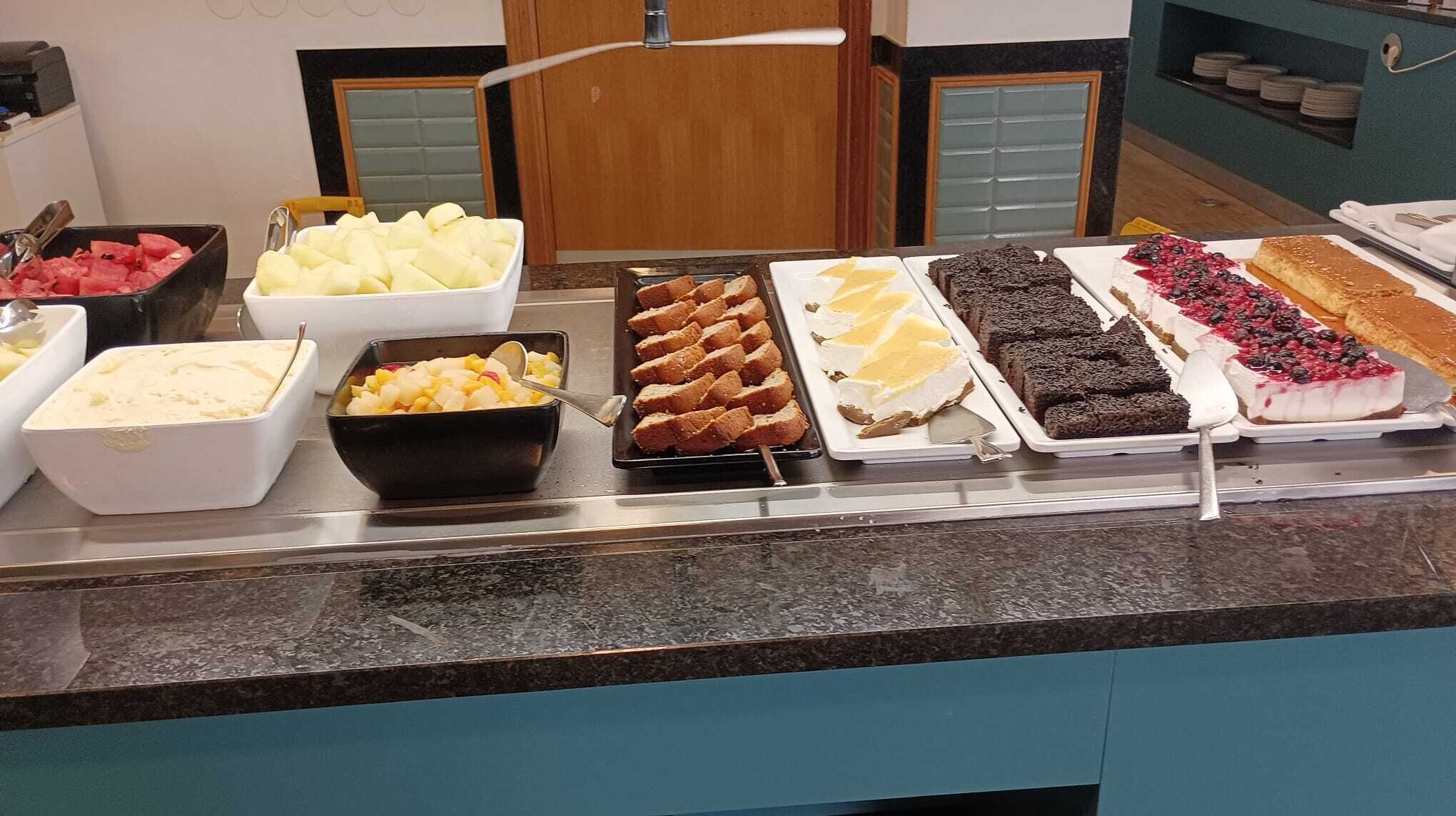 A buffet with various food items including fruits, desserts, and a cake.