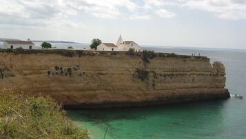 A coastal cliff with a white building featuring a bell tower, overlooking a clear blue sea.