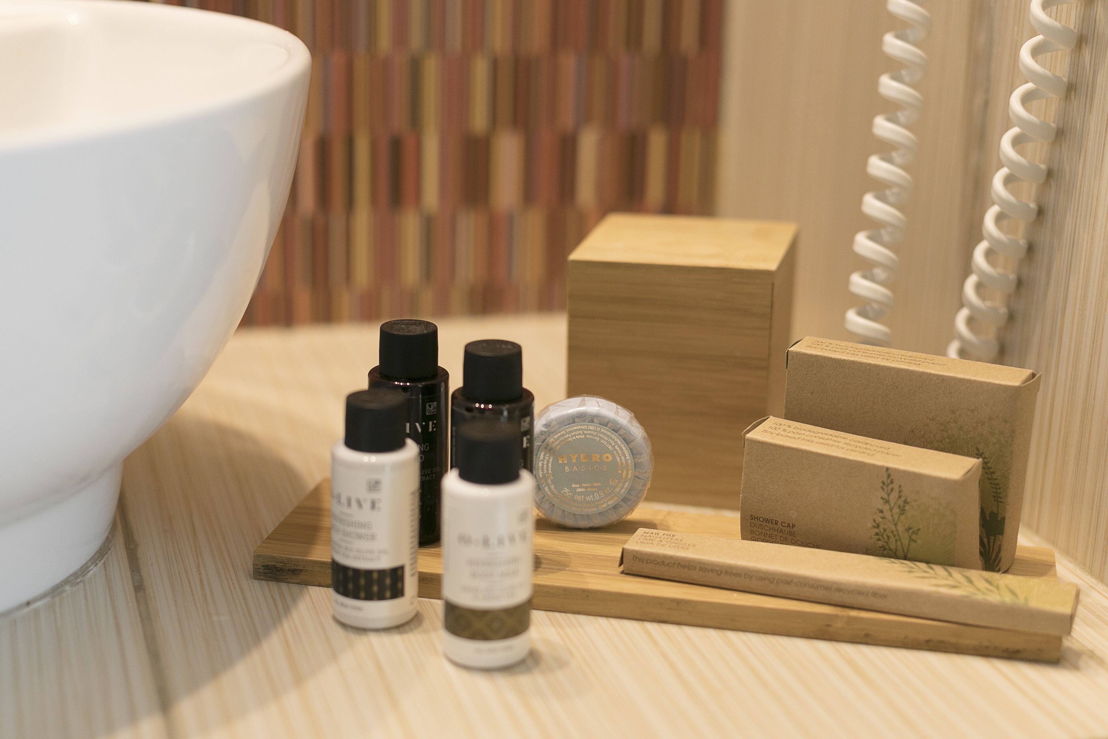 A bathroom vanity with a white basin, wooden tray, and various toiletries including a shower cap and a bottle of liquid soap.