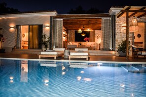 Uma área de piscina moderna ao ar livre, com espreguiçadeiras e cadeiras, uma pérgola de madeira e uma parede de pedra.