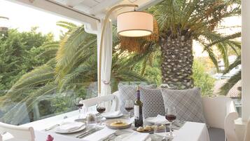 A dining table set for two with a view of palm trees and a house in the background.