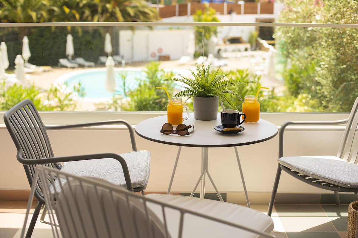 Een balkon met twee stoelen, een tafeltje, een bloempot en twee drankjes.