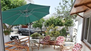 An outdoor seating area with wicker chairs and a green umbrella, surrounded by potted plants and trees. - Skoufezis Studios (Kos)