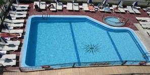 Piscina com espreguiçadeiras e guarda-sóis, rodeada por um deck de madeira.
