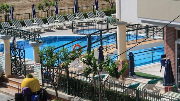 A pool area with lounge chairs and umbrellas, a sign indicating no food or drink in the pool area, and a brick building in the background. - Skoufezis Studios (Kos)