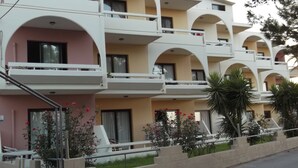 A multi-story hotel with balconies, a pink facade, and a garden area with plants and flowers. - Panorama Studios (Rhodes)