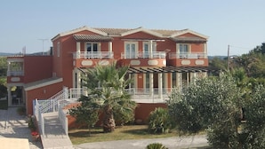 A two-story building with balconies, a covered patio, and a small garden with palm trees. - Aparthotel Orestis (Corfu)