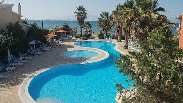 A pool with a curved design, surrounded by lounge chairs and umbrellas, with a view of the sea. - Aparthotel Orestis (Corfu)
