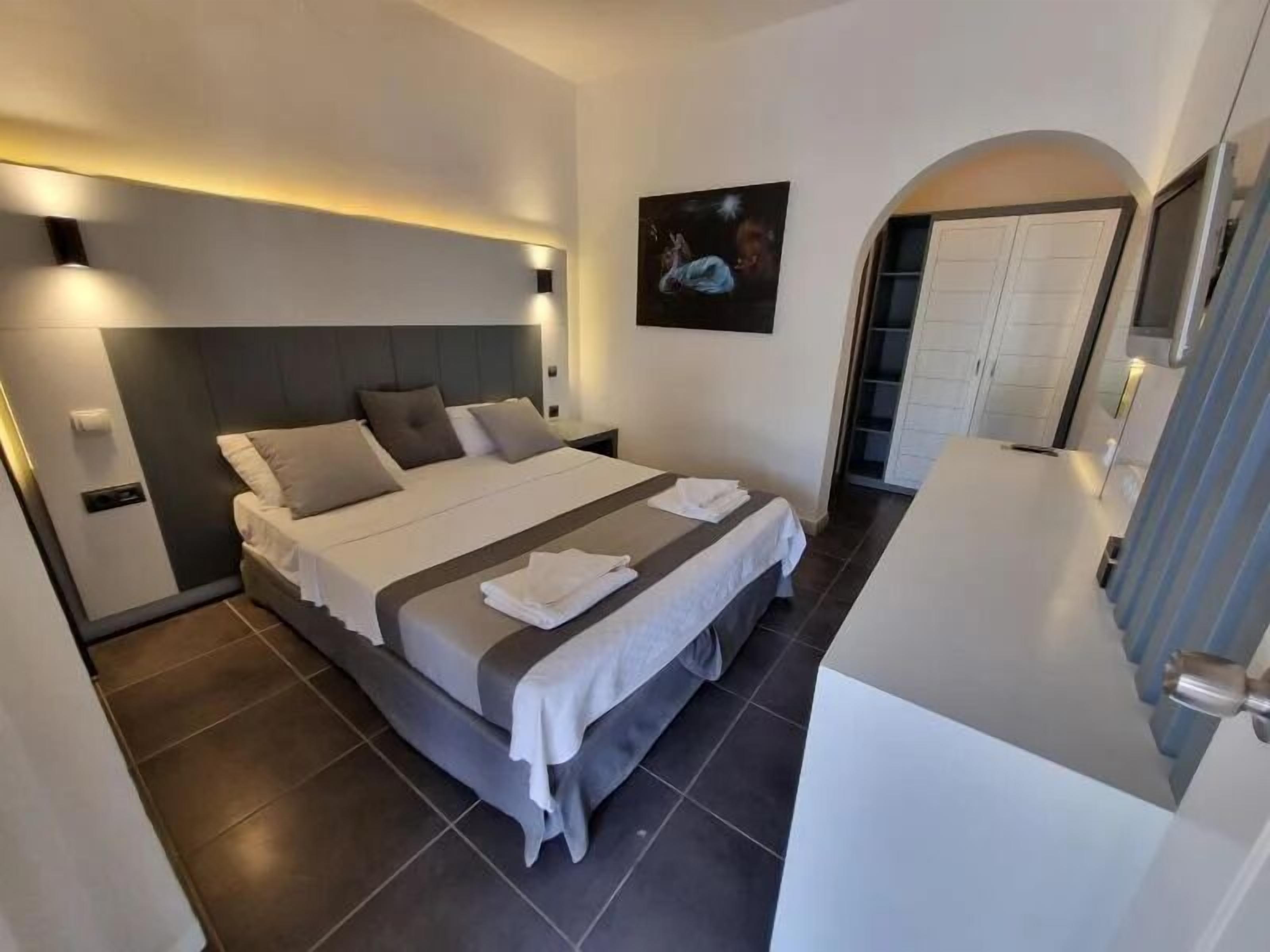 Une chambre d’hôtel moderne avec un grand lit, une table de chevet, une commode, un tableau au mur et une porte de salle de bain.