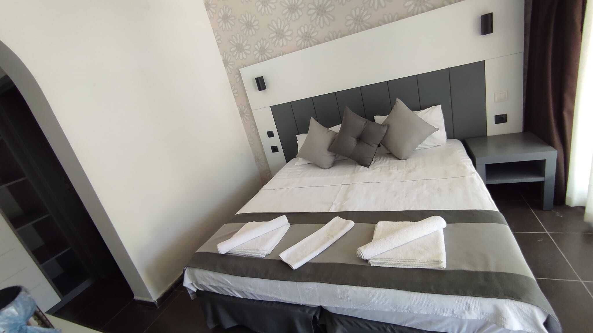 A neatly made bed with pillows and towels, a bedside table, and a nightstand.