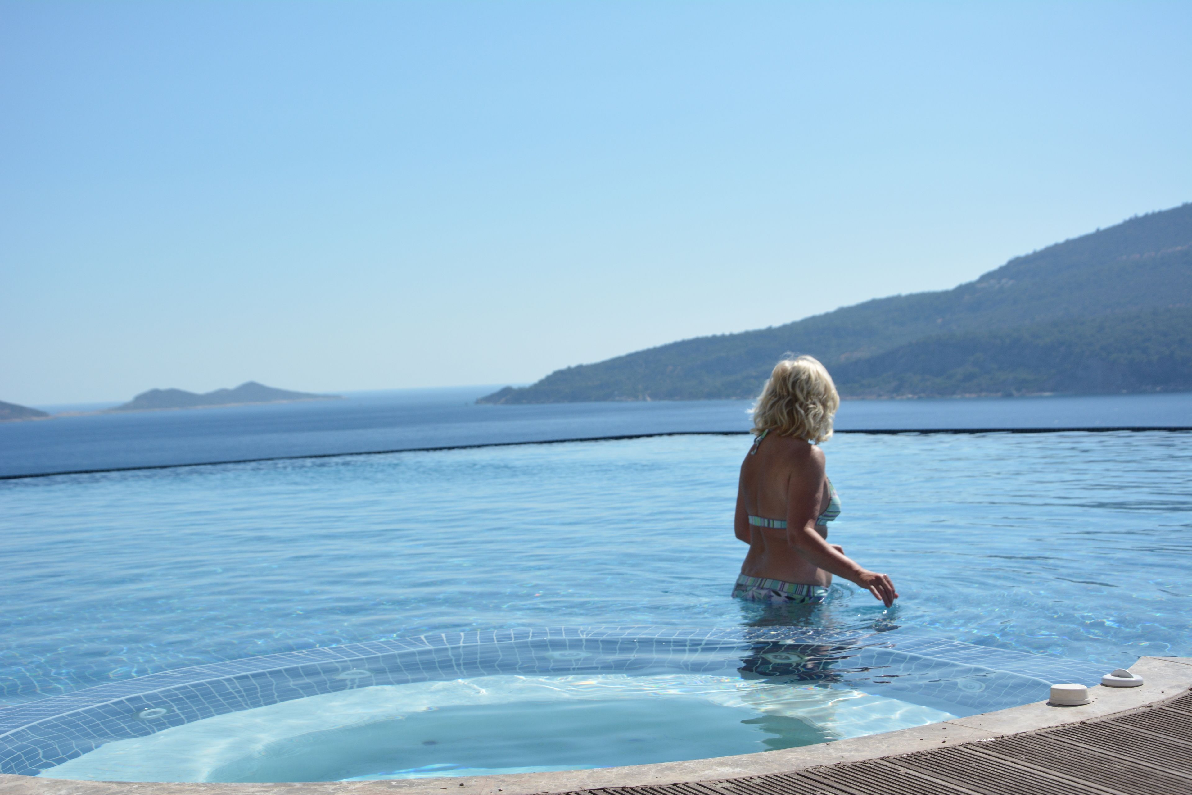 A person in a swimming pool with a view of the sea and hills.