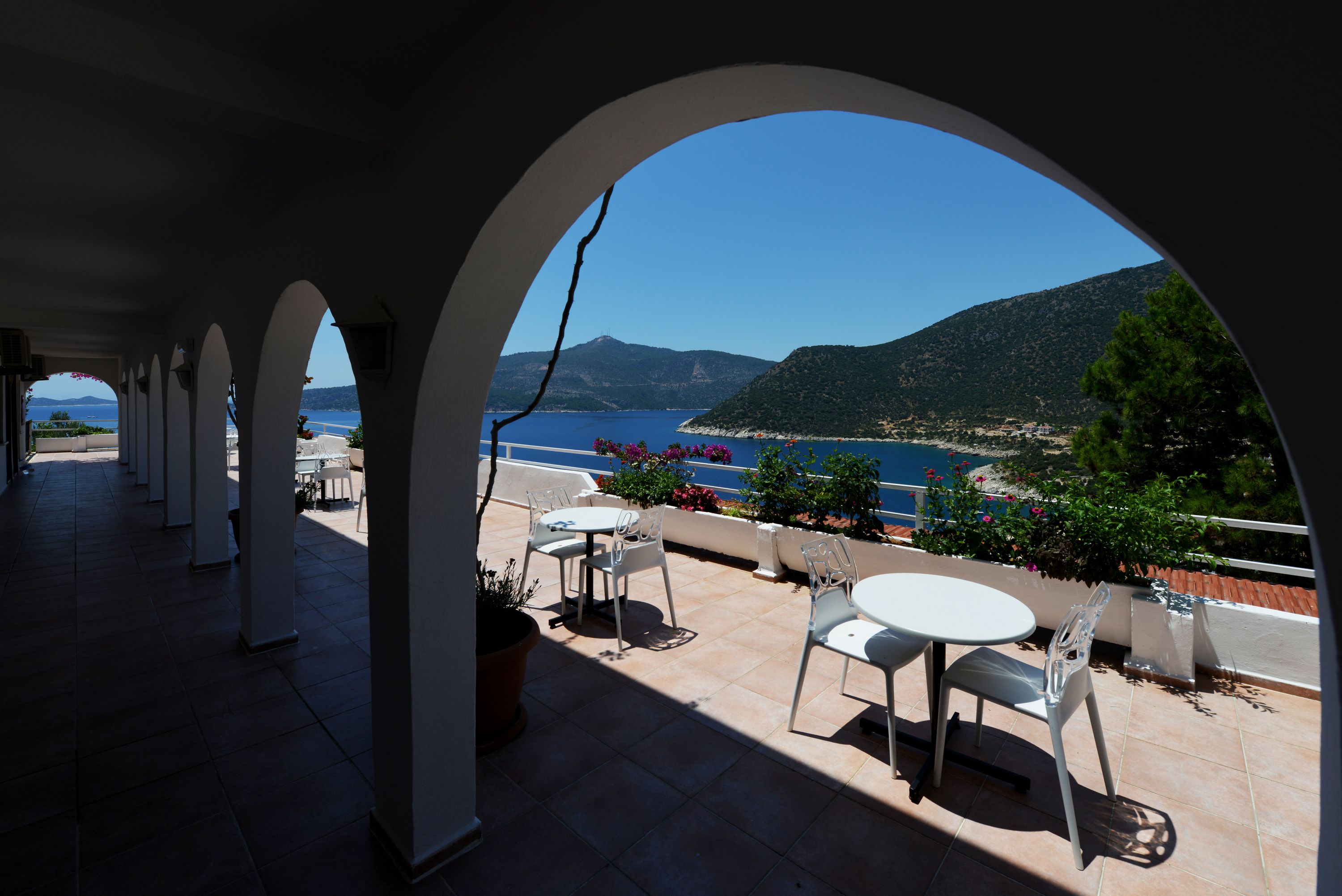 A covered outdoor seating area with a view of the sea and hills.