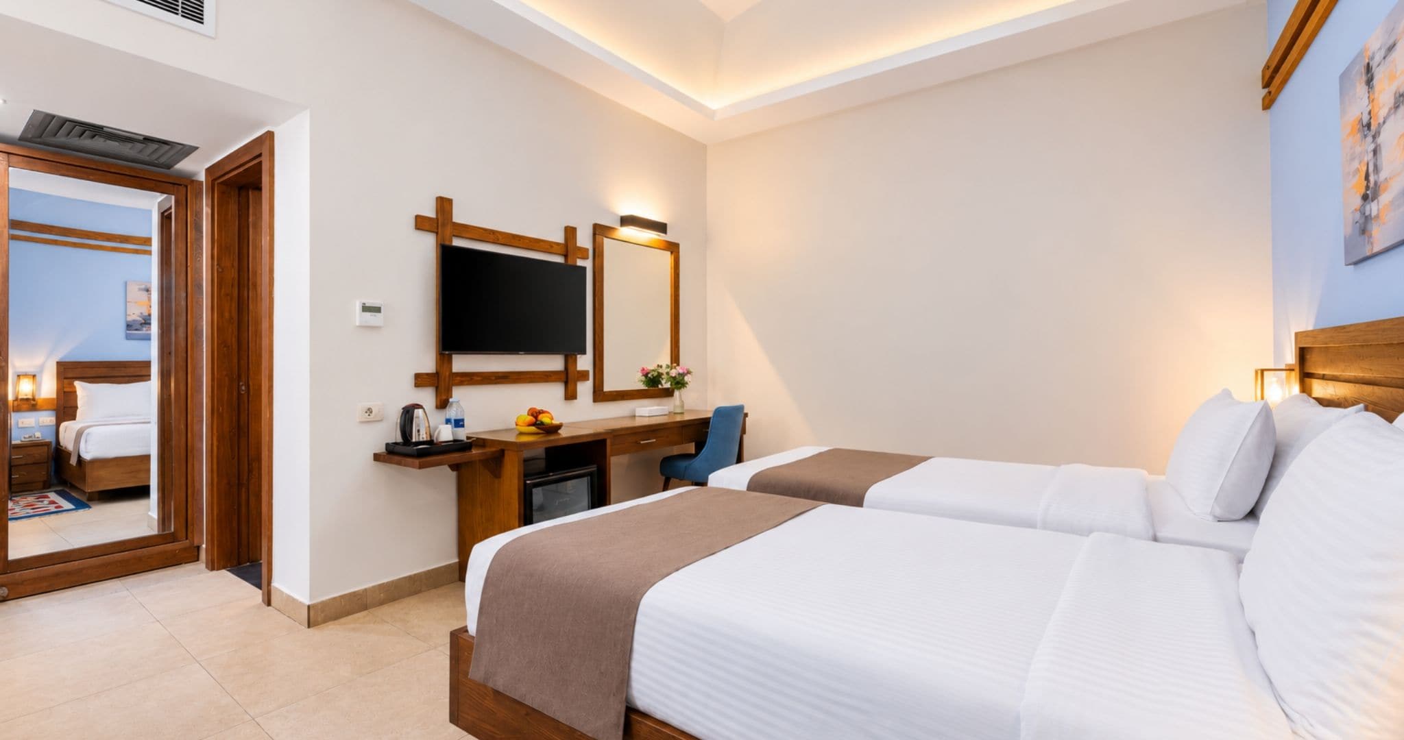 A hotel room with two beds, a desk, a television, and a mirror.