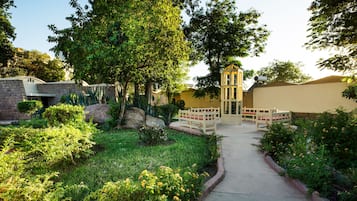 A garden pathway leading to a building with a yellow facade, surrounded by lush greenery and a stone wall.