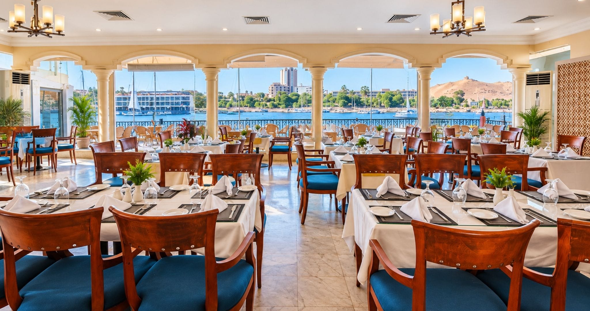 Un restaurante con mesas dispuestas para comer, vistas al agua y un paisaje montañoso al fondo.