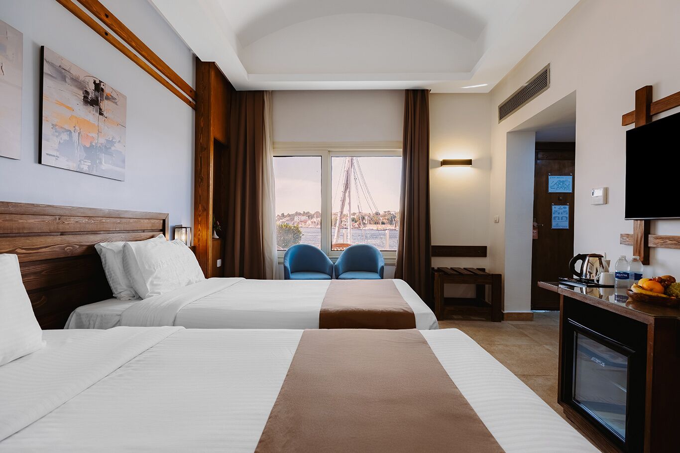 Habitación de hotel con dos camas, un televisor, un escritorio con cafetera y vistas a un puente.
