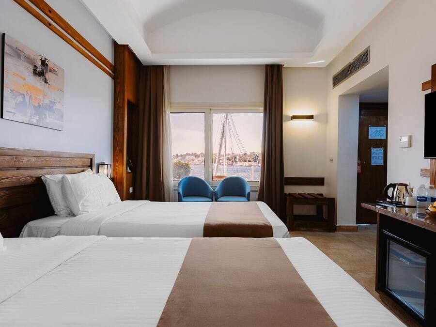 A hotel room with two beds, a TV, a desk with a coffee maker, and a view of a bridge.