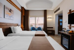 Habitación de hotel con dos camas, un televisor, un escritorio con cafetera y vistas a un puente.