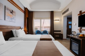 A hotel room with two beds, a TV, a desk with a coffee maker, and a view of a bridge.