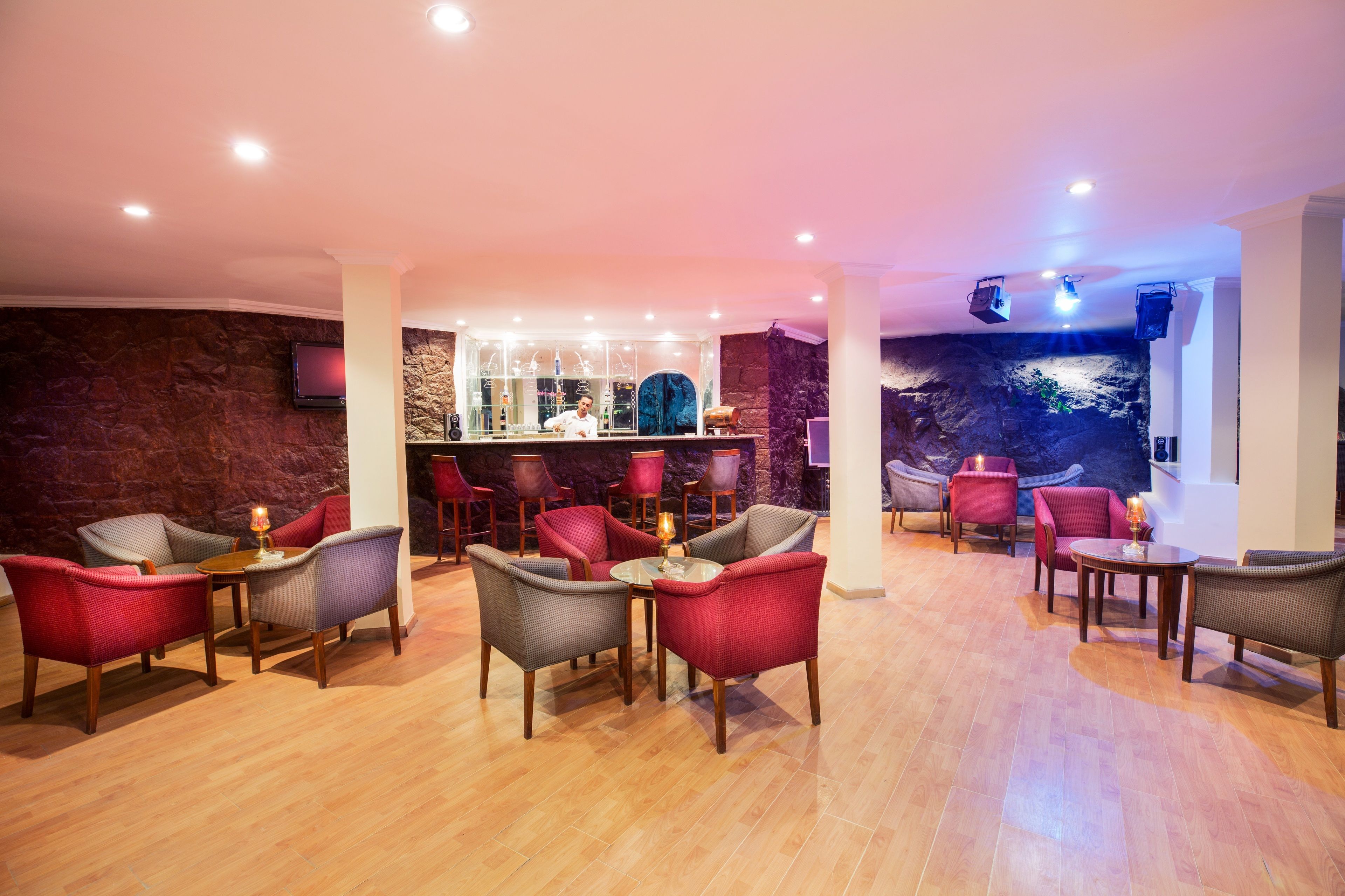 Una hall d'albergo con zona bar, diverse disposizioni di posti a sedere e una parete di pietra sullo sfondo.