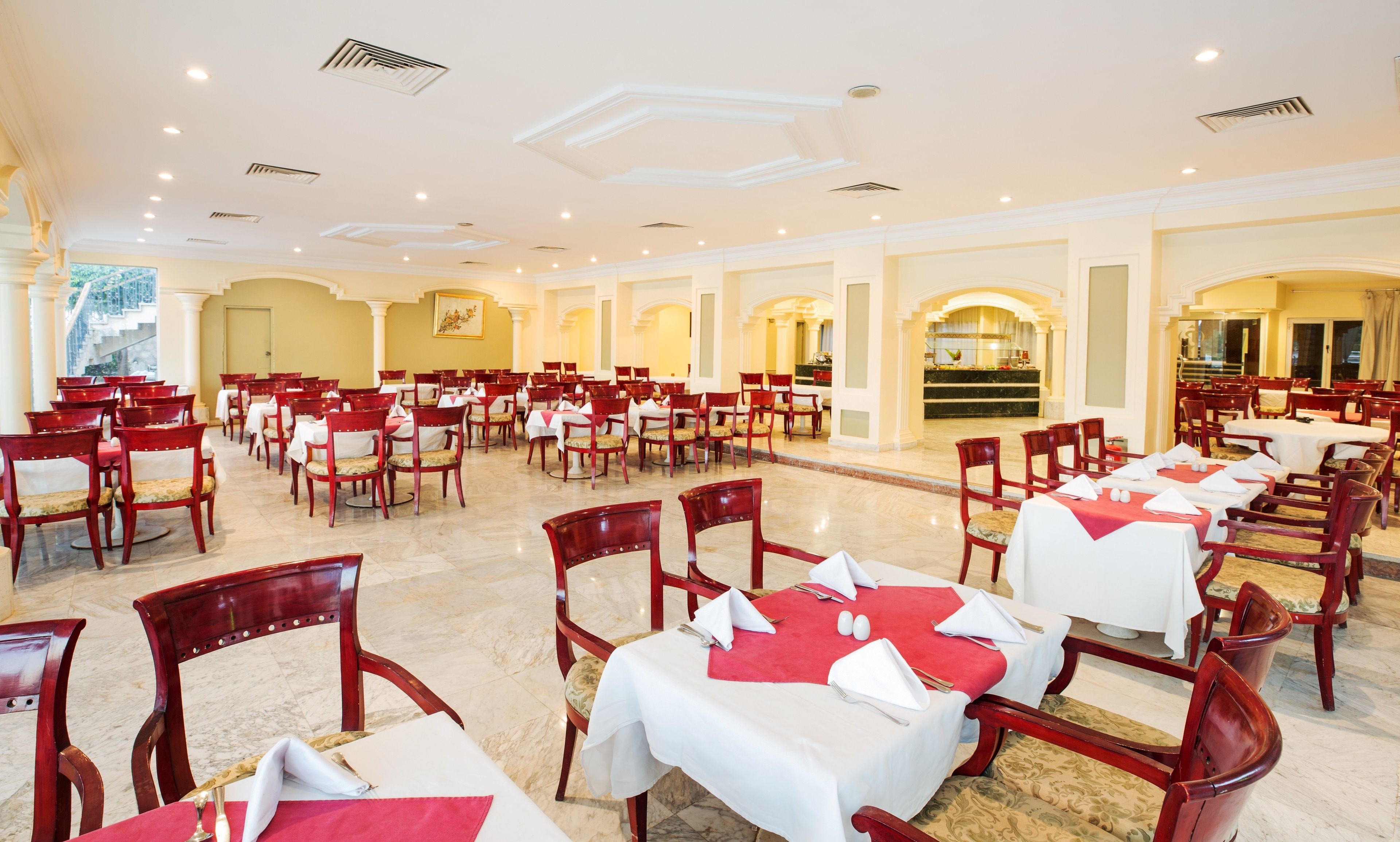 Une grande salle à manger avec de nombreuses tables et chaises, un espace cuisine et un escalier menant à un niveau supérieur.