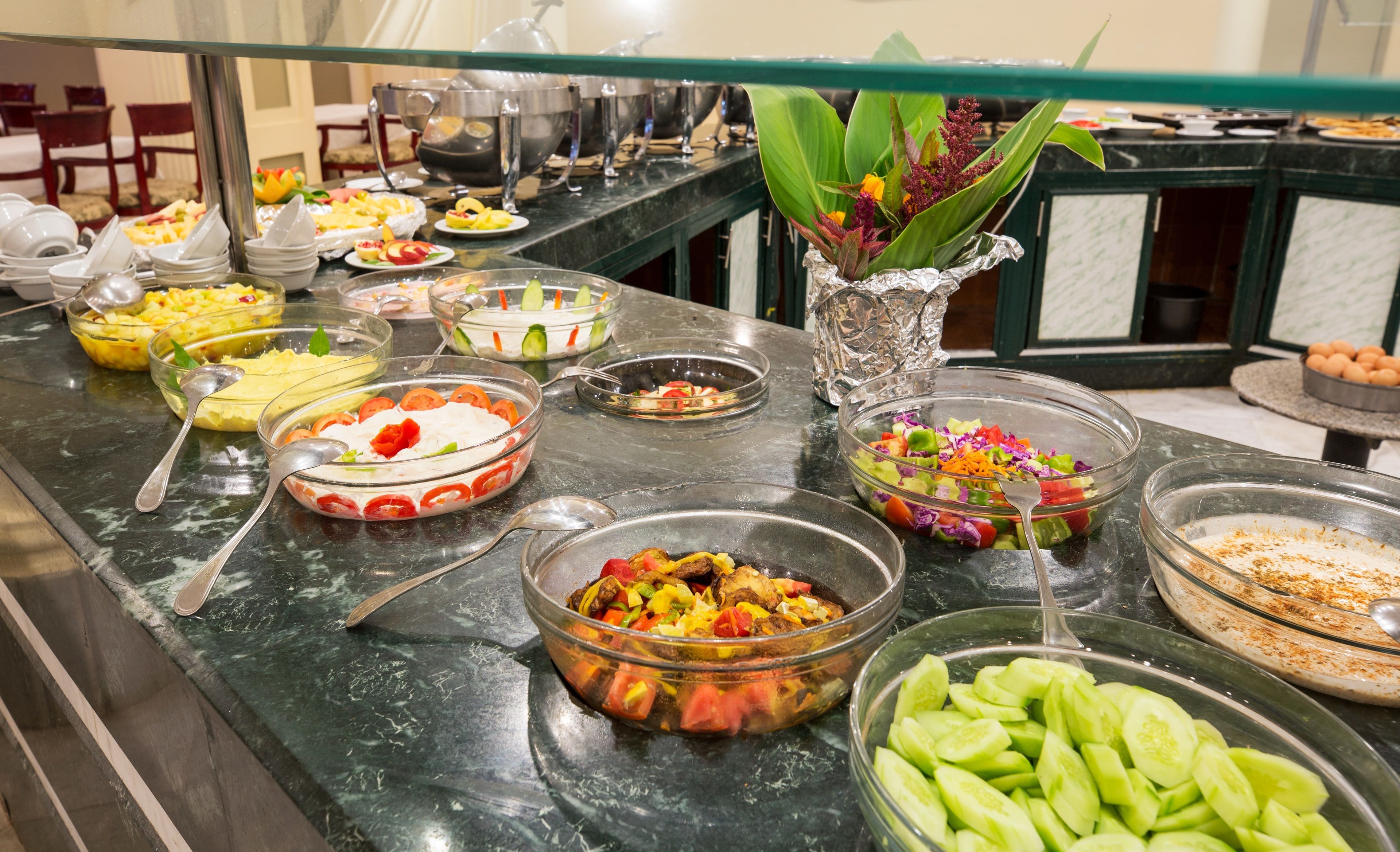 Een buffet met diverse gerechten, waaronder salades, fruit en een bloemstuk.