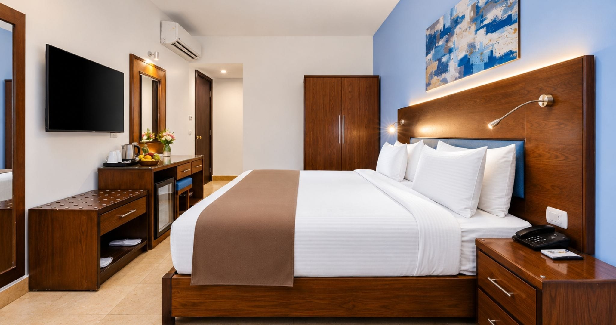 A hotel room with a bed, bedside table, TV, wardrobe, and a painting on the wall.