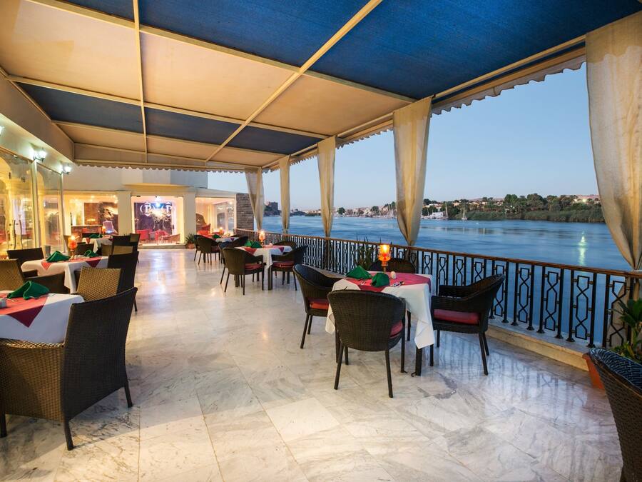 Un restaurante con terraza al aire libre que da a un cuerpo de agua, con mesas y sillas, una zona cubierta y vistas panorámicas del agua.