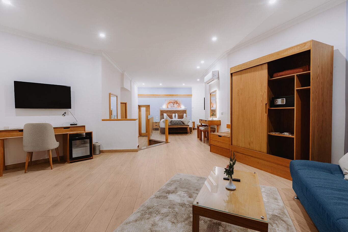 A modern living room with a TV, desk, chair, sofa, and a large wooden wardrobe.