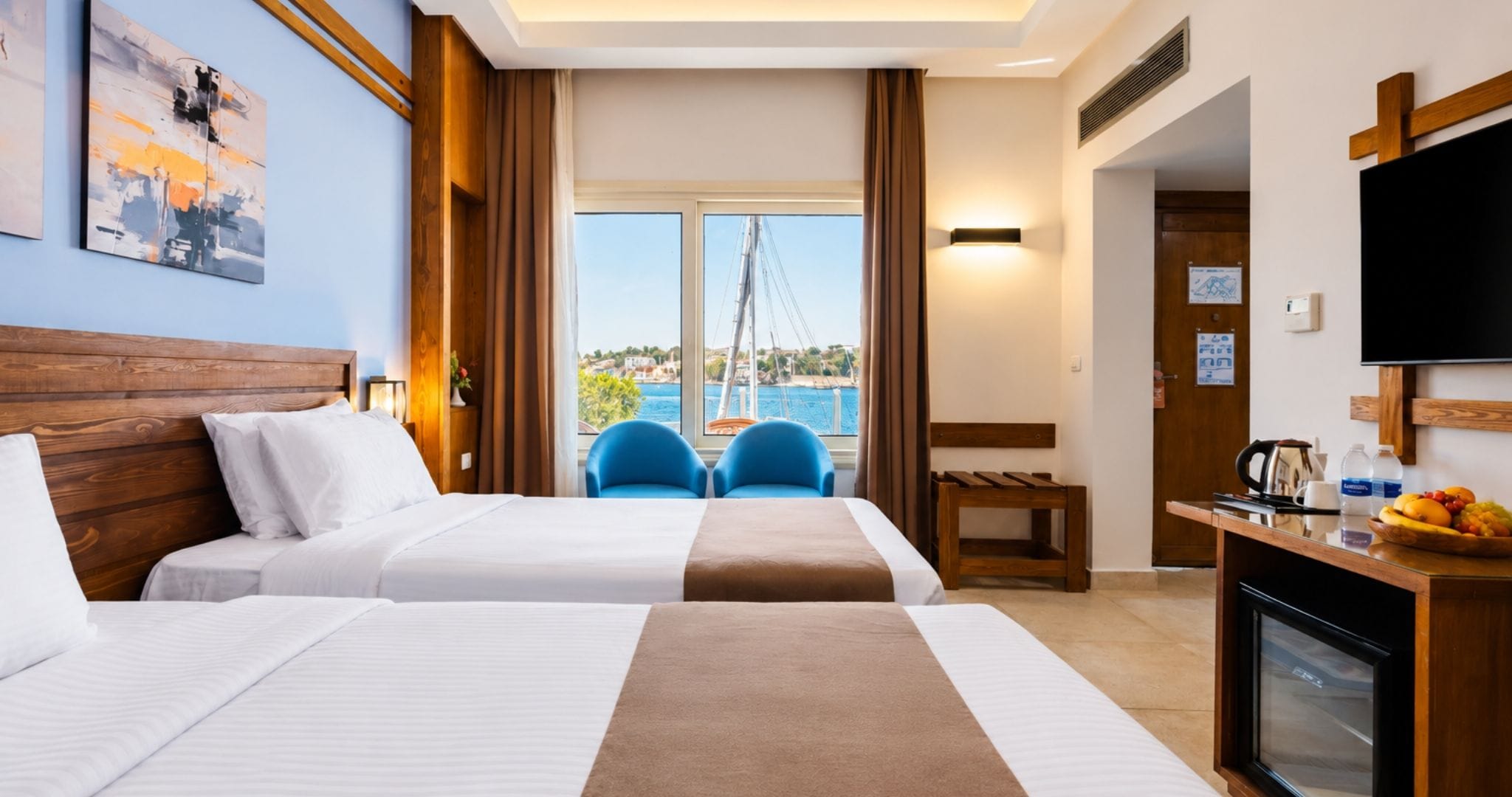 Habitación de hotel con dos camas, un escritorio con cafetera, televisión y vista al mar.