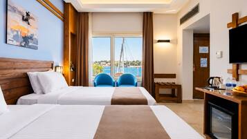 Habitación de hotel con dos camas, un escritorio con cafetera, televisión y vista al mar.