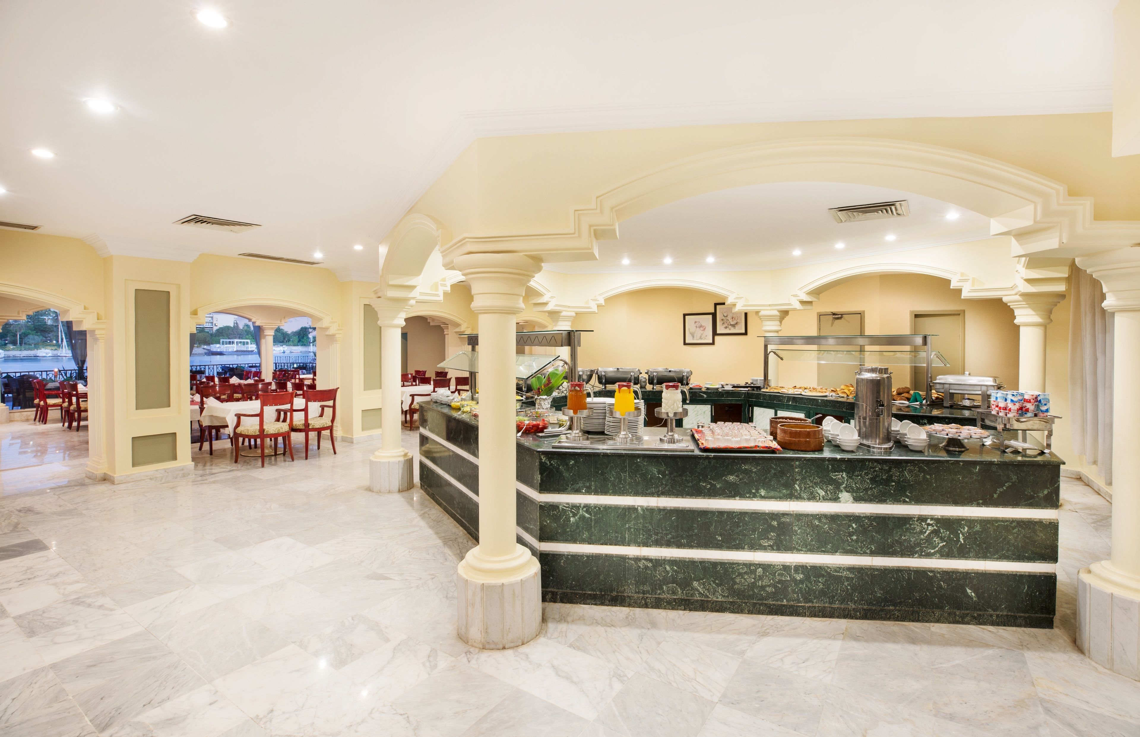 A hotel lobby with a marble floor, a buffet counter, and red chairs.