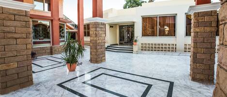 A spacious courtyard with a marble floor, brick pillars, and a potted plant.