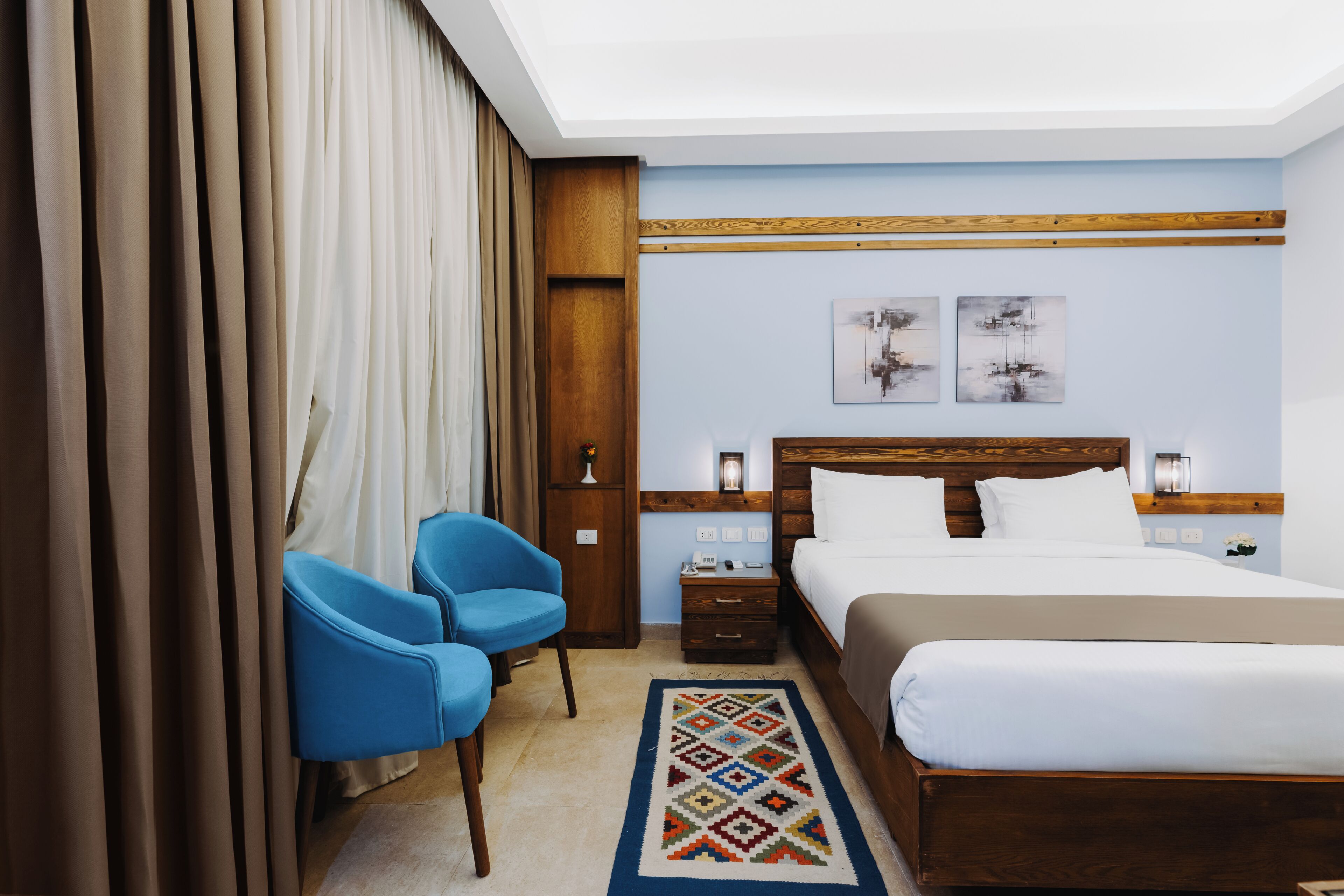 Una habitación de hotel con una cama, una silla azul, una mesita de noche y una lámpara de pared.