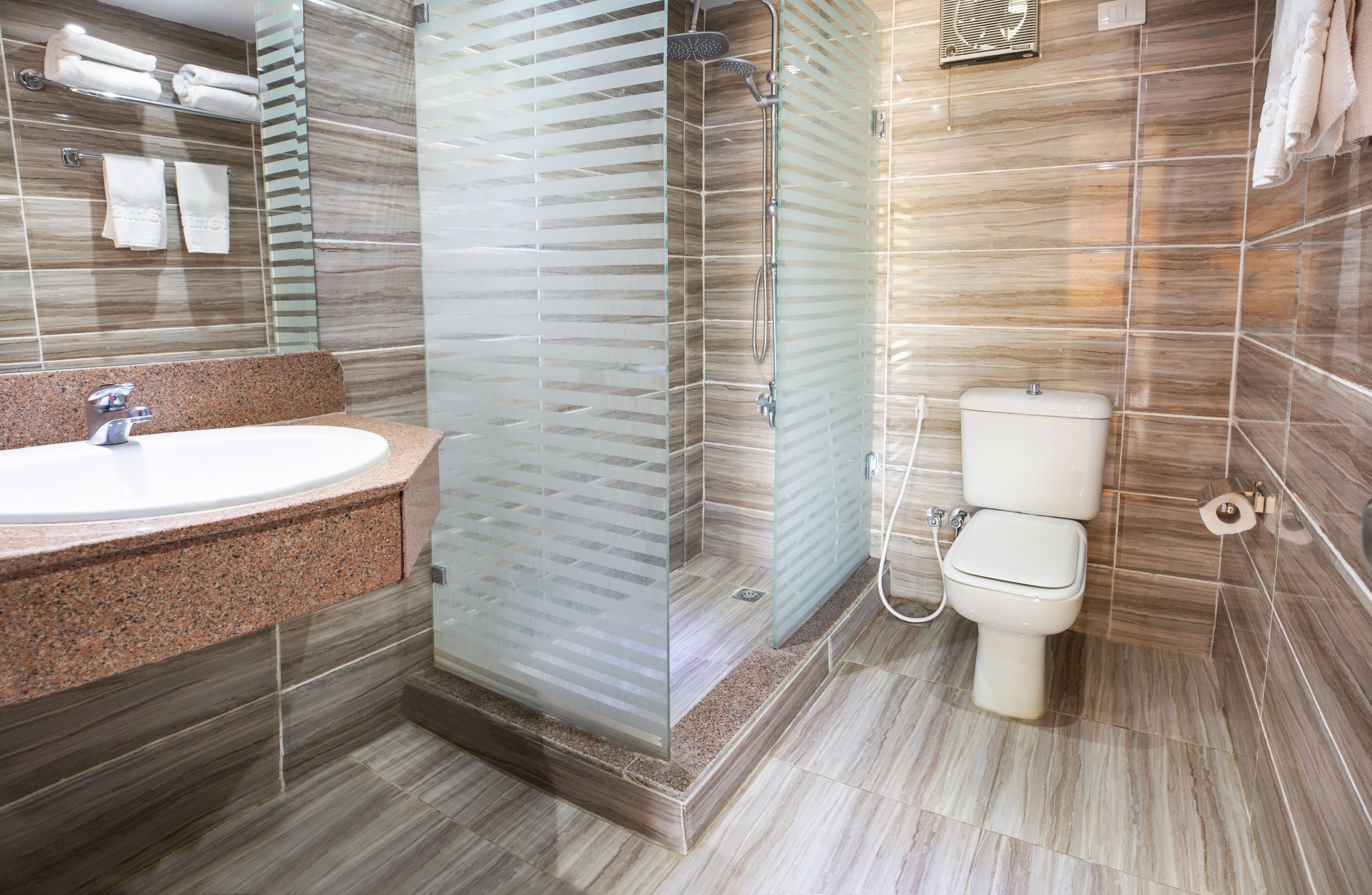 Un baño moderno con lavamanos de encimera de granito, ducha con mampara de vidrio y un inodoro.