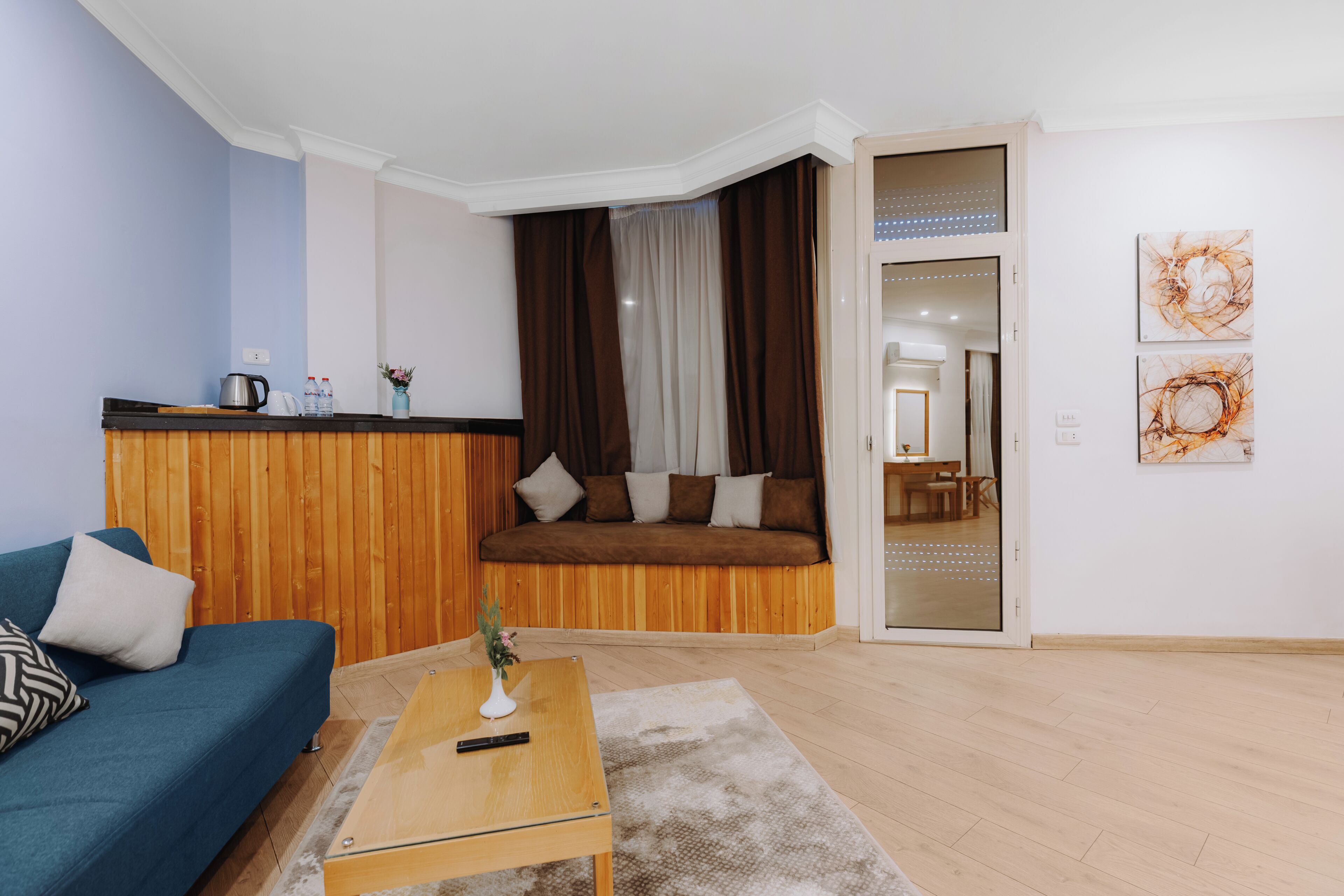 Un salon avec un canapé bleu, une table basse en bois, un canapé marron et une porte en verre donnant sur une autre pièce.