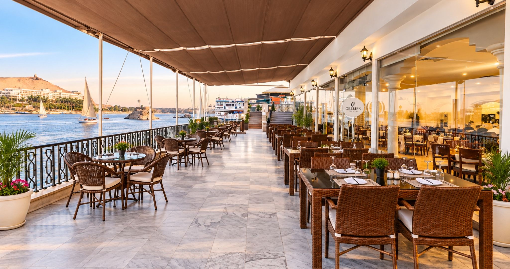 A waterfront restaurant with outdoor seating, a view of the sea, and a mountain in the background.