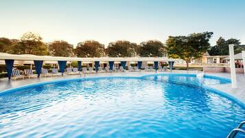 A swimming pool with lounge chairs and umbrellas, surrounded by trees and buildings.