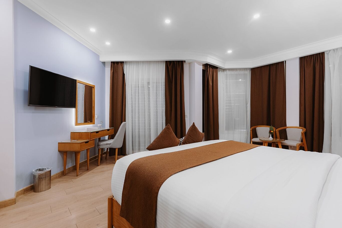 A hotel room with a bed, a desk, a chair, a TV, and a window with curtains.