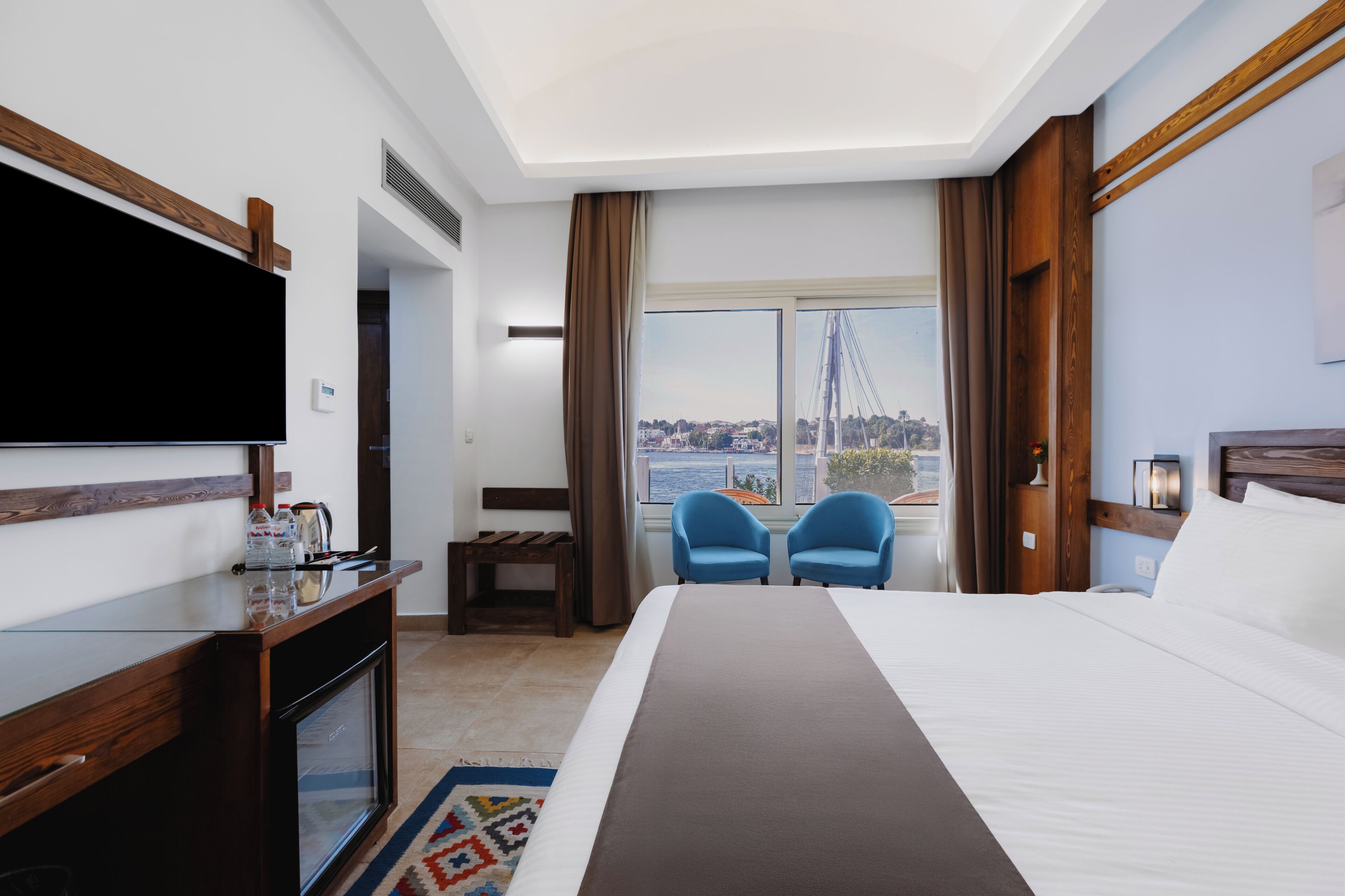 Habitación de hotel con cama, televisión, escritorio, dos sillas, ventana con vista a la ciudad y una vista de un puente.