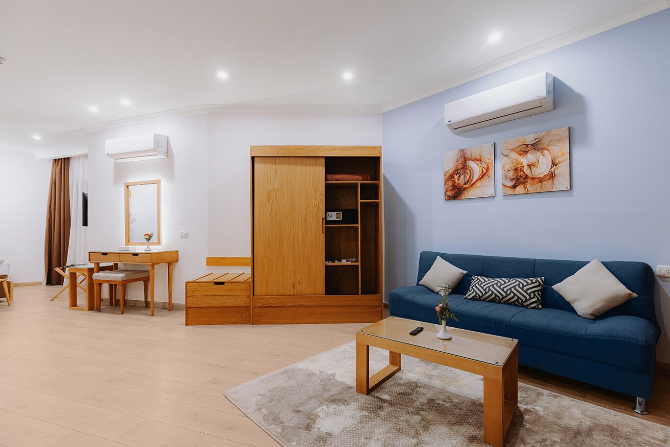 A modern living room with a sofa, a wooden wardrobe, a desk with a chair, and a coffee table.