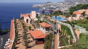 A coastal hotel with a swimming pool, outdoor seating, and a view of the ocean and cityscape. - Hotel Ocean Gardens (Funchal)
